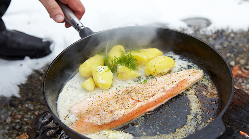 Stekpanna med röding, potatis och dill över öppen eld